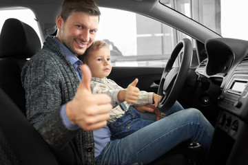 Father and son sitting in car cabin, showing thumbs up.