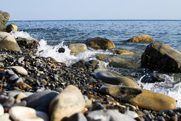 Fototapeta na wymiar the blue waves crashing against the stones lying on the shore of the black sea and dust flying from them