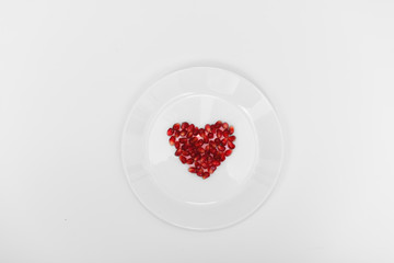 On a white plate from pomegranate seeds composite heart shape. White background. Flat layer.