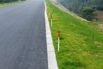 asphalt road and roadside with green grass and red and white pegs