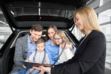 Family buying automobile, man signing document of purchase.