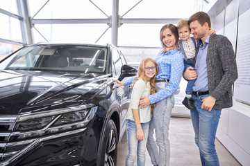 Family posing near black auto in dealership showroom.