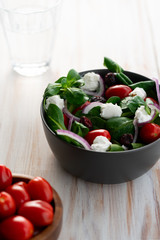Winter salad with lamb's lettuce, spinach, cherry tomatoes, red onion, dried cranberries and goat cheese. Grey ceramic bowl, white wooden table, high resolution