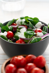 Winter salad with lamb's lettuce, spinach, cherry tomatoes, red onion, dried cranberries and goat cheese. Grey ceramic bowl, white wooden table, high resolution