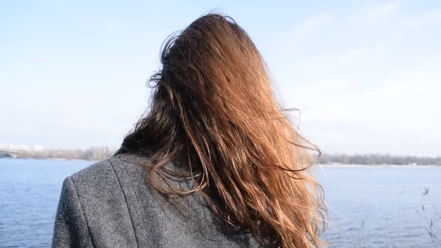 Rear view of the lush hair of a young woman on the background of the river in the city.