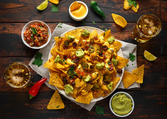 Mexican nachos tortilla chips with olives, jalapeno, guacamole, tomatoes salsa, cheese dipand beer.