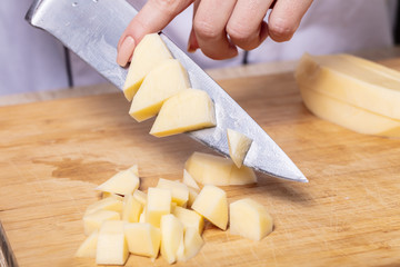 cook cuts potatoes on a wooden board