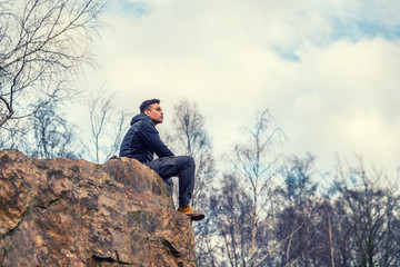 A young guy who is out and hiking in outdoor clothing in a nature reserve stands and looks out over...