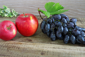 Blue grapes and red apples on wooden background