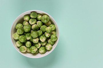 Fresh uncooked brussel sprouts in a bowl on minty green background. Photo with blank free space.