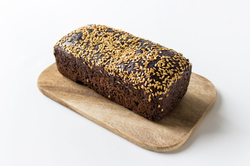 Loaf of rye bread with sesame seeds on a wooden board on white background.