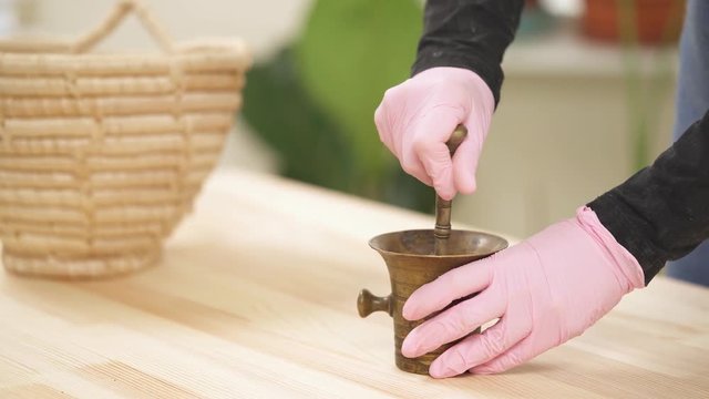 Close-up view, a girl grinds dried rose petals in a copper mortar with pestle. Process of making natural facial scrub.