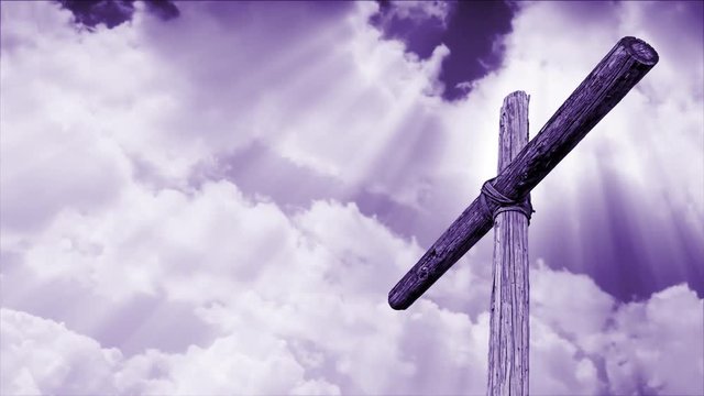 An old rugged wooden cross is backed by motion clouds with rays of shining light from above in shades of violet purple.