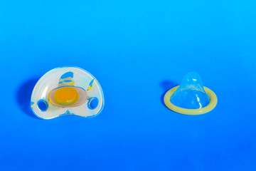 Naklejka premium Baby nipple and condom on blue background, concept of healthy sex and the birth of children.