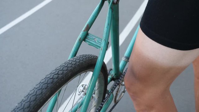 Close up view of a green track fixed retro bicycle on a velodrome and a cyclist leg with sun tun 