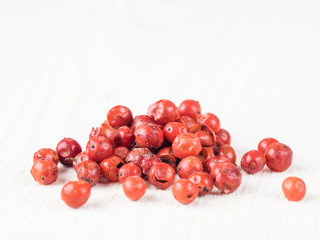 Heap of dried pink pepper berries on white wooden table. Close up view of pink peppercorn. Copy space.