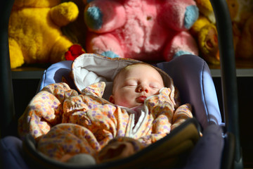 A newborn baby lies and sleeps in a stroller against the background of children's soft toys.
