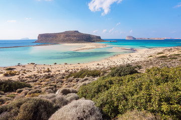 Obraz premium The white sand beside the sea, where the bottom can be seen, the beach with people. Beautiful mountains on a blue horizon. Incredible Balos. A landscape on a summer sunny day. Crete Island, Greece.