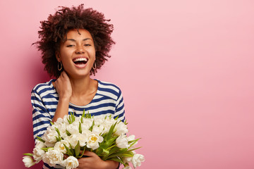 Emotive pleased black woman expresses happiness, wears sailor casual jumper, smells scent of white...