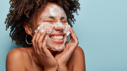 Sideways shot of pleasant looking lady applies cosmetic foam, feels pleasure after beauty...