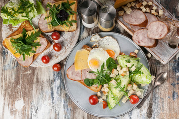 Healthy breakfast and snacks. Fried eggs, chicken ham sandwich, ice salad, cherry tomatoes and arugula. Top view
