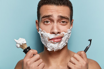 Cropped shot of attractive man with gel on cheeks, has sad expression, tired of shaving very often,...