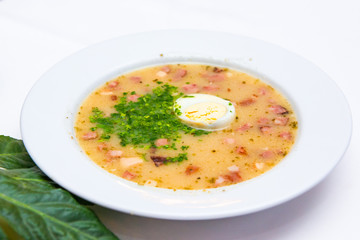 Traditional polish white borscht - zurek, sour soup with white sausages and eggs.
