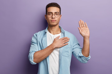 Honest serious hipster guy swears to do something, keeps hand on chest, gestures with palm,...