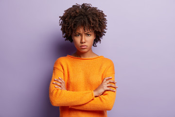 Angry sad young black female model crosses hands over chest, looks with grumpy expression, wears...