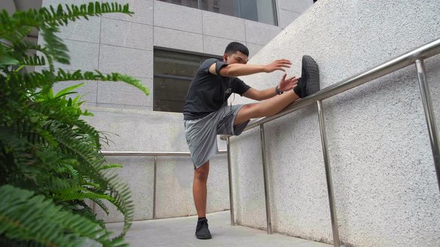 Wide shot of Asian sporty man doing warm up of his legs outdoors