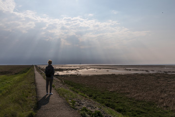 Fototapeta premium Person geht dem Licht entgegen auf dem Trischendamm in Friedrichskoog Spitze
