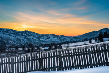 Wooden fence overlooking a small mountain village at sunrise in winter