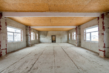 Unfinished apartment or house big loft room under reconstruction. Plywood ceiling, plastered walls, window openings, cement floor. Construction and renovation concept.