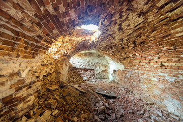 Old forsaken empty basement room of ancient building or palace with cracked plastered brick walls, low arched ceiling, small windows with iron bars and dirty floor.