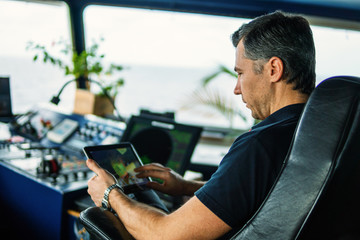 Marine chief officer or captain on navigation bridge watching digital tablet. Internet and home...
