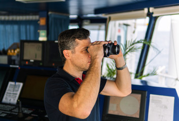 Fototapeta na wymiar Navigational officer lookout on navigation watch looking through binoculars. Marine industry. COLREG collision regulations