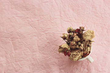 Dry roses in white cup on a pink paper background. Author processing, film effect.