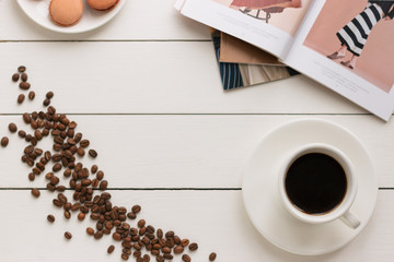 Cup of black coffee on a white wooden table with coffee grains and fashion magazine. Author processing, film effect.