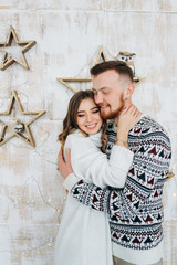 Sweet cute young and happy couple hugging near white wall decorated garland and wooden stars