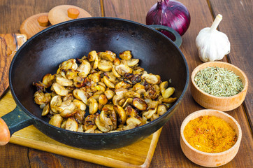 Black cast iron pan with fried mushroom slices on wooden background.