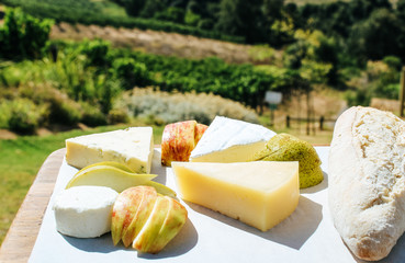Assorted cheese platter with various cheeses on a wooden board in front of a vineyard.
