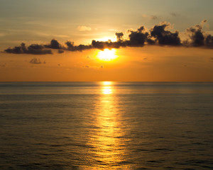 Golden sunset with clouds over ocean and reflection in water