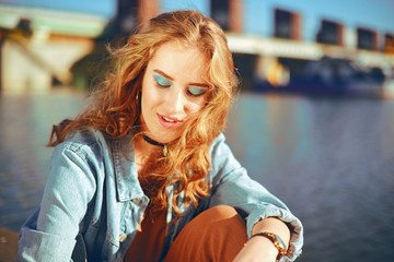 Beautiful girl sitting on the pier near the river. Hipster blonde model with gorgeous  cerly hair....