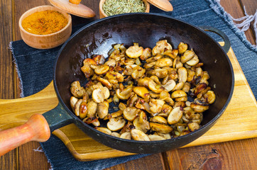 Black cast iron pan with fried mushroom slices on wooden background.