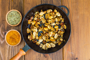 Black cast iron pan with fried mushroom slices on wooden background.