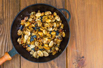 Black cast iron pan with fried mushroom slices on wooden background.