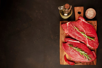 raw New York steaks with ingredients on a chopping board. on the background of dark stone. with copy space