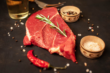 A big raw New York steak with ingredients. on the background of dark stone.