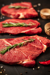 big raw new york steaks with ingredients. on the background of dark stone.