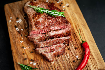 Ready to eat New York black angus steak with ingredients on a cutting board. Ready meal for dinner on a dark stone background.